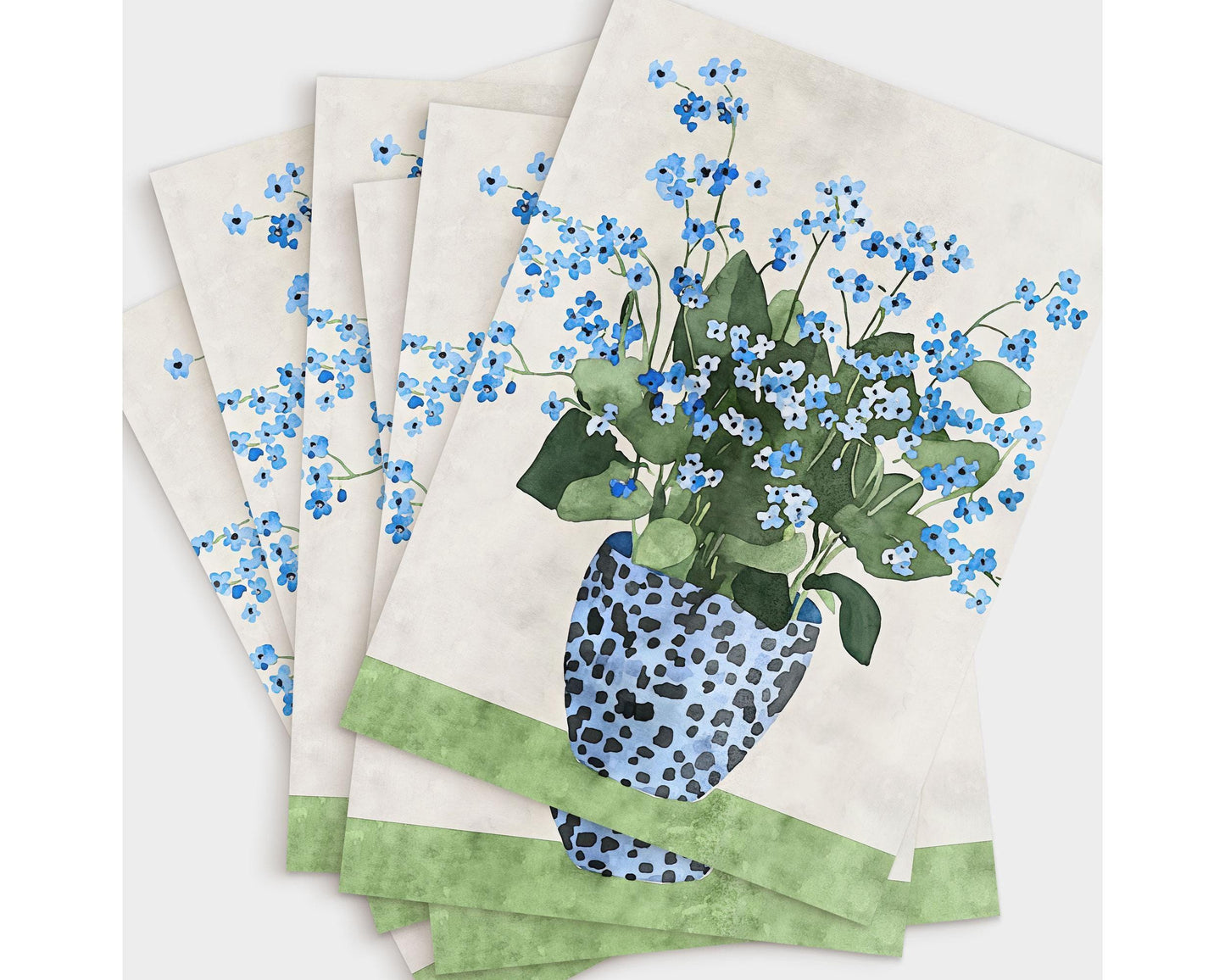 Set of greeting cards fanned out in a stack, each featuring a watercolor illustration of blue forget-me-nots in a spotted blue vase on a green surface with a soft beige background.