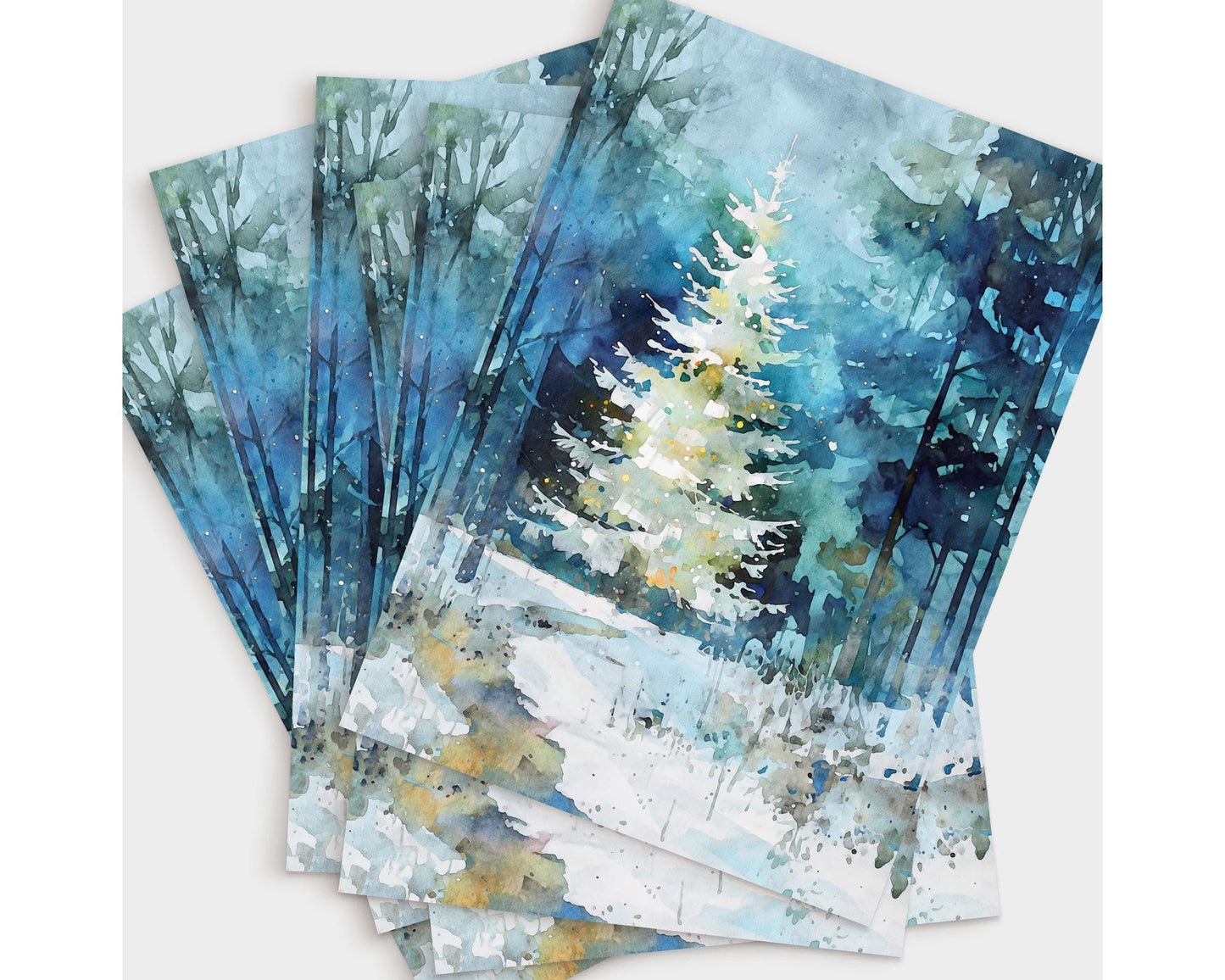 A fanned stack of greeting cards featuring a watercolor-style painting of a glowing white Christmas tree in a snowy blue-green forest. The layered cards highlight the soft washes, tall tree silhouettes, and gentle winter light that create a serene, festive atmosphere.