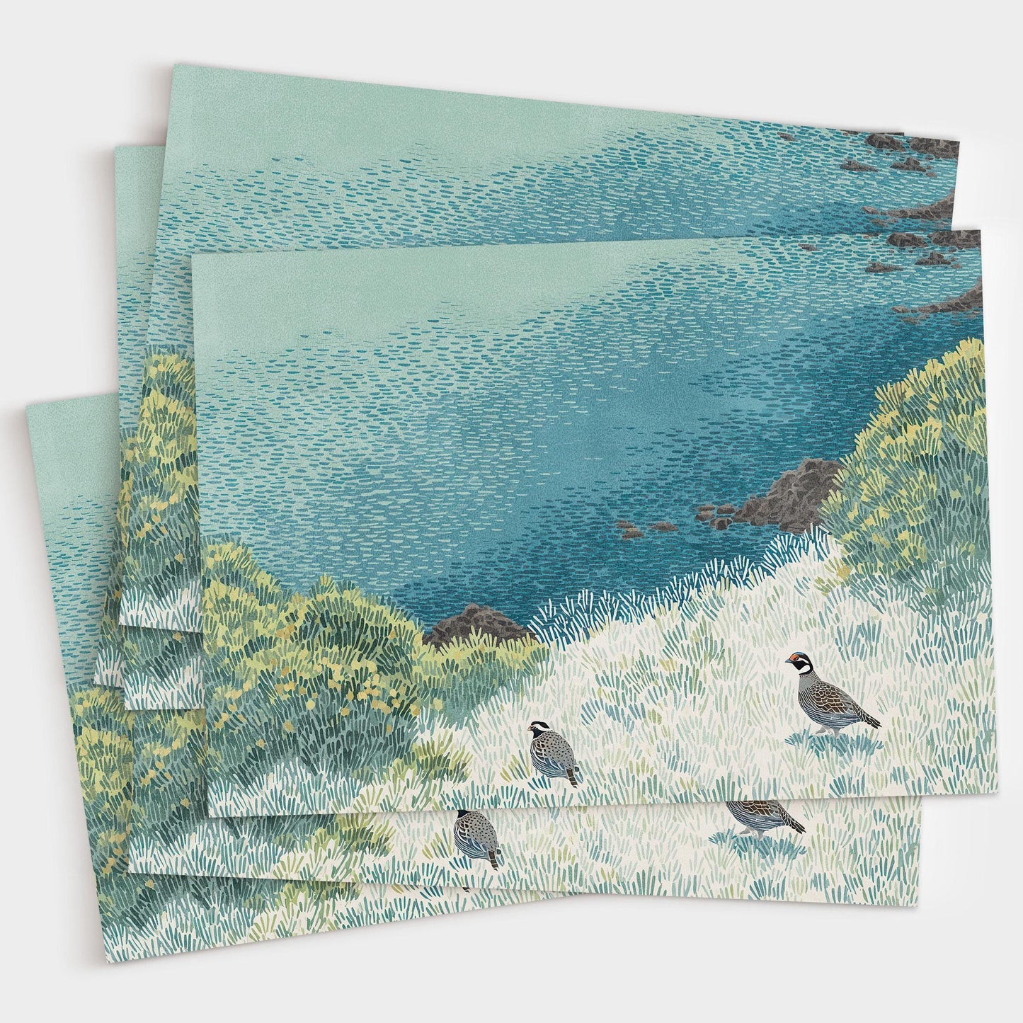 Stack of greeting cards featuring an illustration of two quail in a grassy coastal landscape with layered blue, green, and yellow textures. The cards are slightly fanned out on a white background, showcasing the detailed artwork and consistent design.