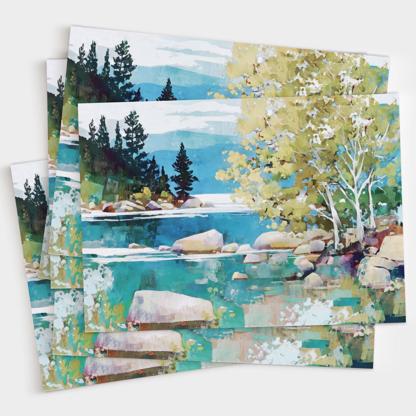 Set of greeting cards featuring a vibrant impressionist landscape of a turquoise lake with smooth boulders, birch trees with pale trunks and green foliage on the right, and dark evergreens against distant blue mountains under a cloudy sky. The cards are slightly fanned out to show multiples.