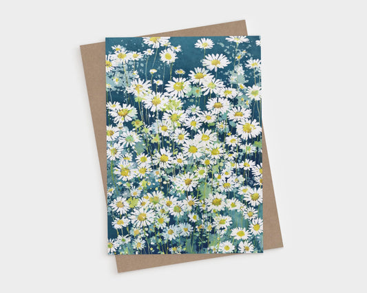 Watercolor-style greeting card featuring a lush field of white daisies with yellow centers against a deep blue-green background, evoking a fresh, summery garden scene. The card rests on a brown kraft envelope, displayed on a white surface.