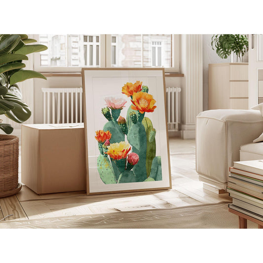 Framed watercolor art print of a cactus with colorful blooms in orange, yellow, pink, and red, leaning against a box in a bright, modern living room with plants, books, and large windows.