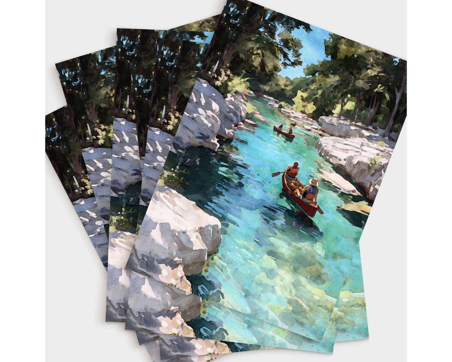 Set of greeting cards featuring a watercolor-style painting of two red canoes on a clear turquoise river, framed by rocky white banks and green trees under a bright blue sky, fanned out in a layered display.