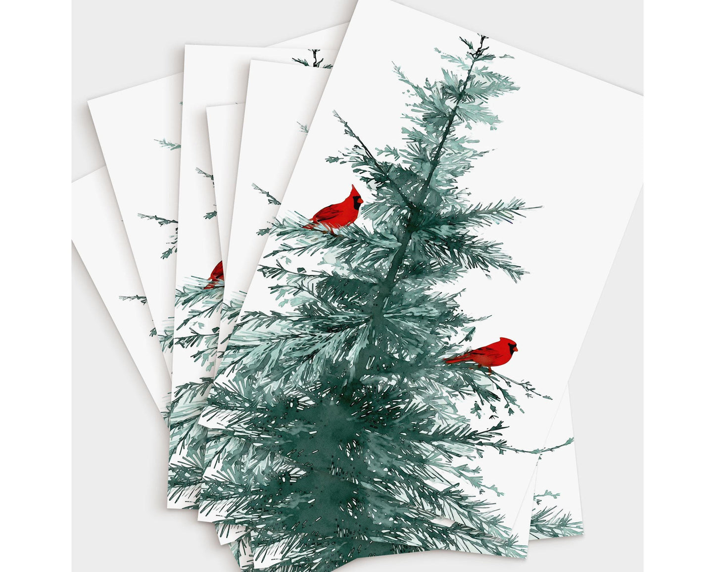 Set of greeting cards featuring a watercolor illustration of a pine tree with two bright red cardinals perched on its branches, fanned out to display multiple copies on a white background.