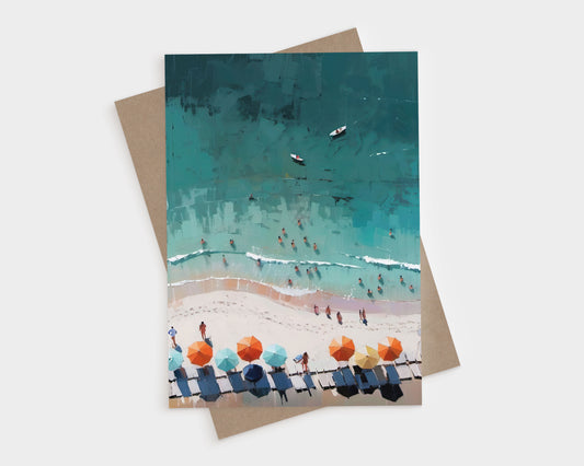 Greeting card featuring an aerial illustration of a beach scene with people in the water, colorful umbrellas, and lounge chairs on the sand; shown with a kraft brown envelope beneath.