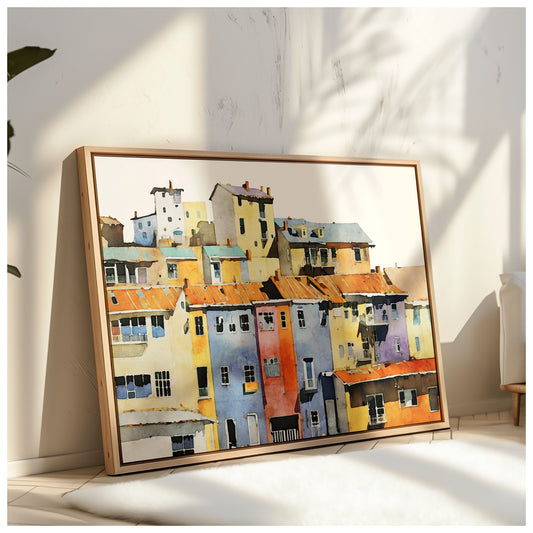 Framed watercolor painting of a colorful hillside village with vibrant buildings, leaning against a textured wall in a sunlit room.