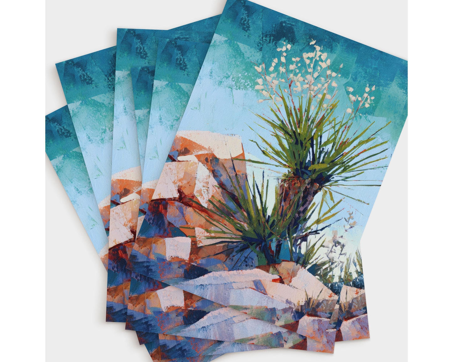 Set of greeting cards featuring a vibrant desert painting of a yucca plant with spiky green leaves and delicate white blossoms, surrounded by red and orange rocky terrain under a vivid blue sky.