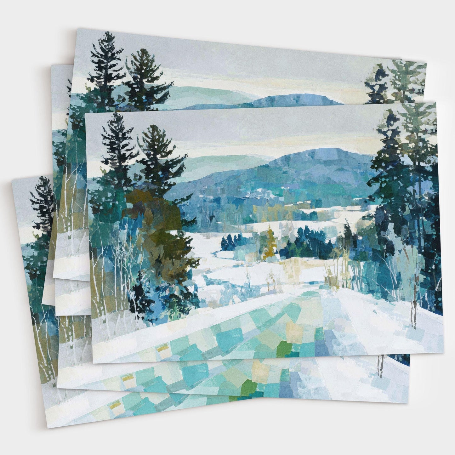 Set of greeting cards featuring a winter landscape painting with snowy hills, evergreen trees, and distant blue mountains in cool tones of teal, green, and white.