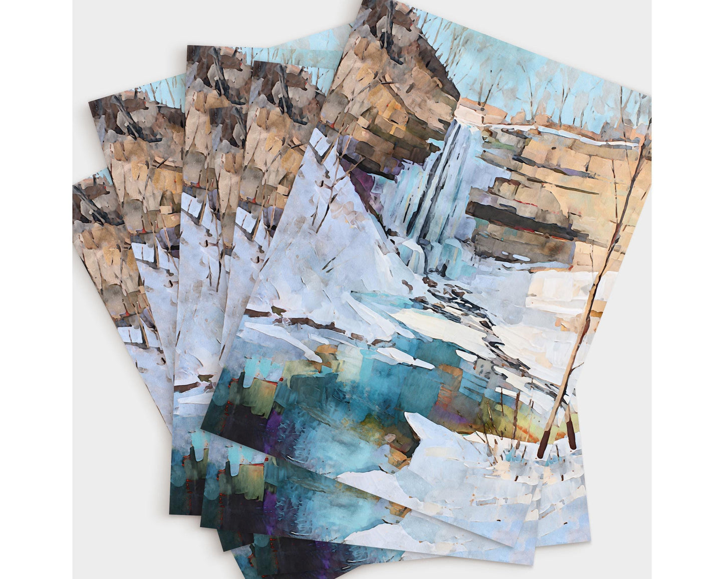 Set of greeting cards displayed in a fanned arrangement, each featuring a watercolor-style painting of a snowy winter waterfall scene. The artwork shows a cascade flowing over rocky cliffs into a turquoise pool, surrounded by snow and bare trees under a pale sky.