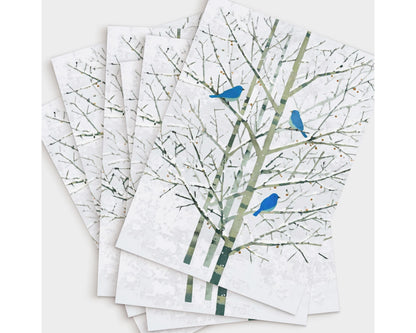 Set of greeting cards featuring a minimalist watercolor-style illustration of three bluebirds perched on pale winter branches. The cards are fanned out on a white background, showcasing the delicate green-gray trees and vivid blue birds that create a serene, nature-inspired design.