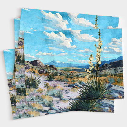 Set of greeting cards featuring a watercolor-style desert landscape with blooming yucca plants, rocky hills, and distant mountains under a bright blue sky with fluffy clouds, fanned out in a layered stack.