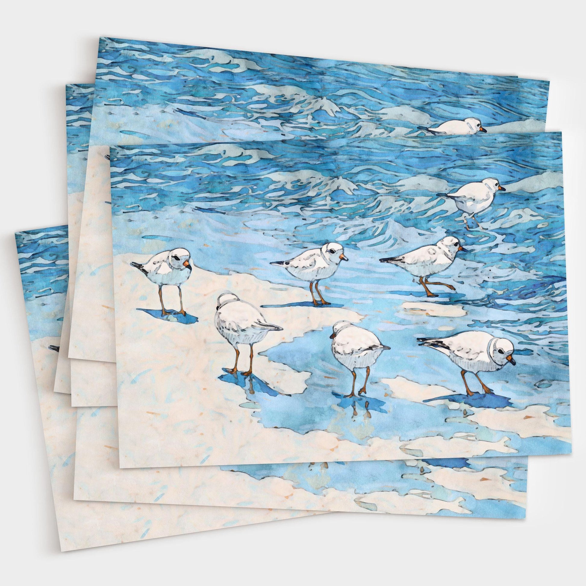 Set of greeting cards featuring a watercolor-style illustration of small white shorebirds with orange legs standing on sand and wading in rippling blue ocean water, shown stacked slightly fanned out against a white background.