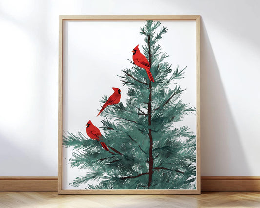 Framed art print featuring an illustration of three bright red cardinals perched on the branches of a green pine tree, displayed in a light wood frame against a white wall and wood floor.