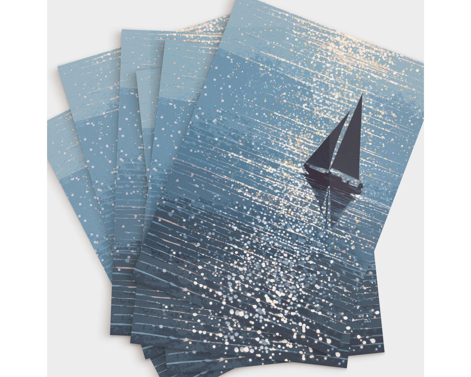 Set of five greeting cards fanned out on a light surface, each featuring a sailboat silhouette gliding through shimmering blue water with scattered sunlight reflections. The artwork has a soft, painterly texture and coastal palette, perfect for ocean lovers or nautical-themed occasions.