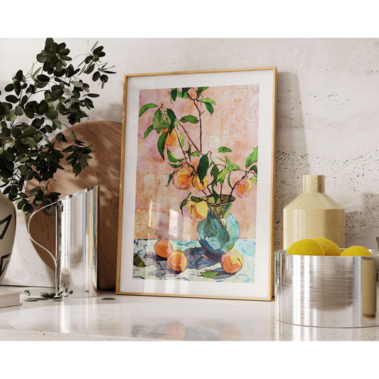 Framed still life painting of peaches in a blue glass vase, styled on a modern shelf with decorative objects. The artwork features leafy branches and ripe peaches against a pink textured background. Surrounding decor includes a ceramic vase with greenery, a tall pitcher, a cutting board, a yellow vase, and a silver bowl of lemons, creating a warm, contemporary setting.