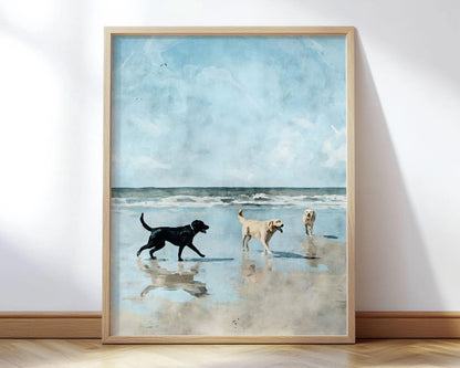 Framed watercolor-style print of three Labrador retrievers playing on a sandy beach, with ocean waves and a blue sky in the background. A black lab walks toward two yellow labs, one carrying a stick, all reflected in the wet sand.