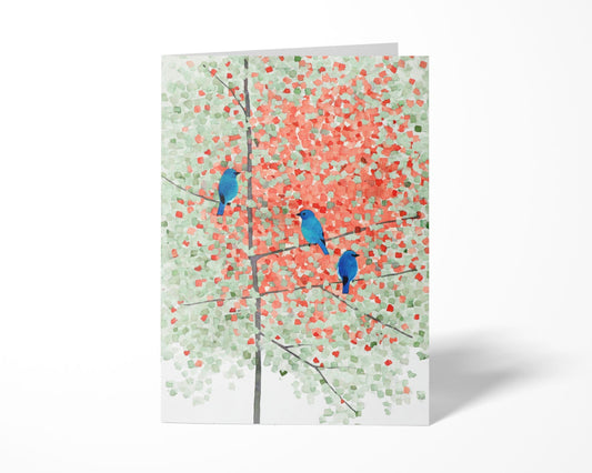 Folded greeting card featuring a watercolor painting of three bright bluebirds perched on slender branches of a maple tree with soft green and red-orange leaves, evoking early autumn. The impressionistic design blends cool and warm tones against a white background for a calm, nature-inspired look.