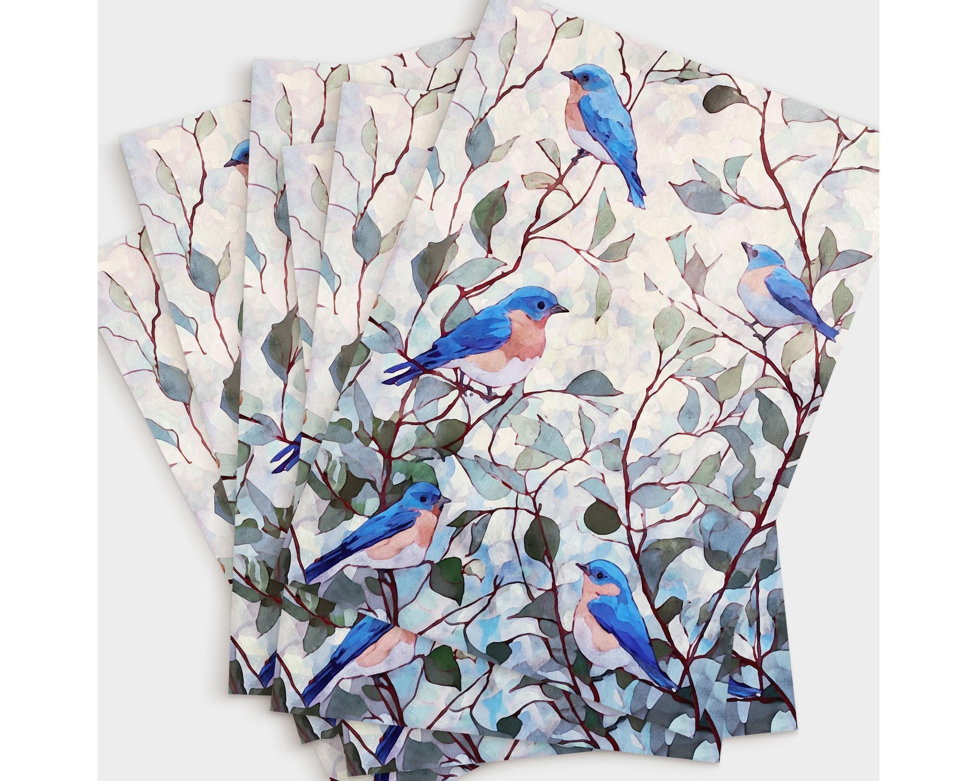 Set of greeting cards featuring a watercolor design of bluebirds with peachy chests perched on red-brown branches with soft green leaves against a pale, dappled background, fanned out in a neat stack.