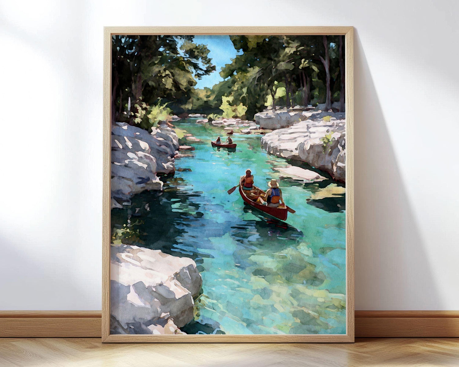 Framed watercolor-style painting of two people canoeing on a clear turquoise river surrounded by white stone cliffs and green trees, with another canoe in the distance under a bright blue sky.