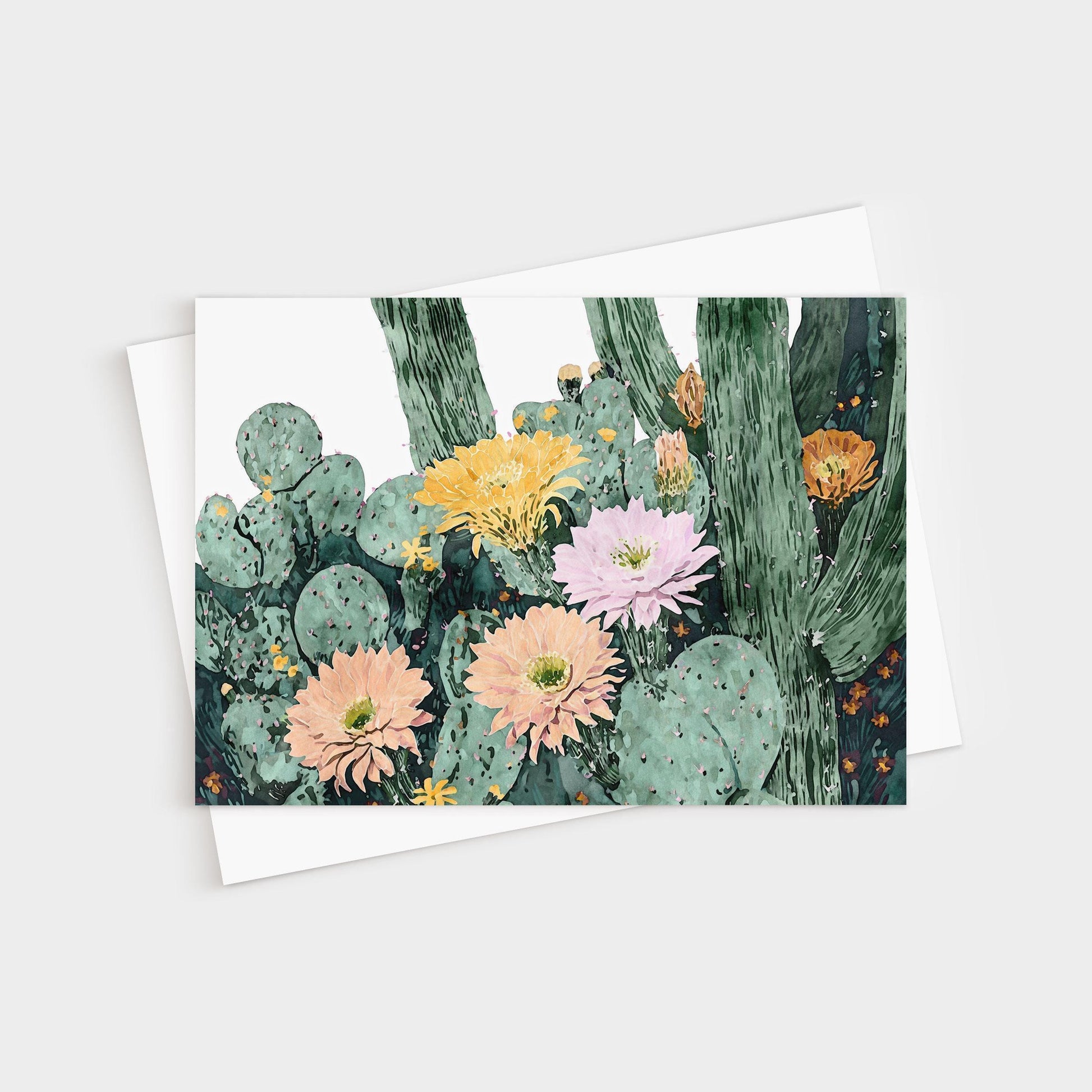 Greeting card featuring a watercolor illustration of blooming cacti with large flowers in soft peach, pink, yellow, and orange tones against green cactus pads and tall stems, paired with a white envelope.