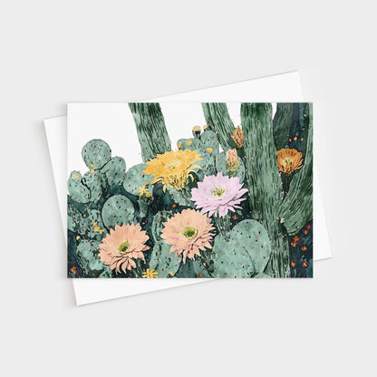 Greeting card featuring a watercolor illustration of blooming cacti with large flowers in soft peach, pink, yellow, and orange tones against green cactus pads and tall stems, paired with a white envelope.