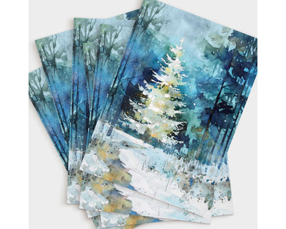 A fanned stack of greeting cards featuring a watercolor-style painting of a glowing white Christmas tree in a snowy blue-green forest. The layered cards highlight the soft washes, tall tree silhouettes, and gentle winter light that create a serene, festive atmosphere.