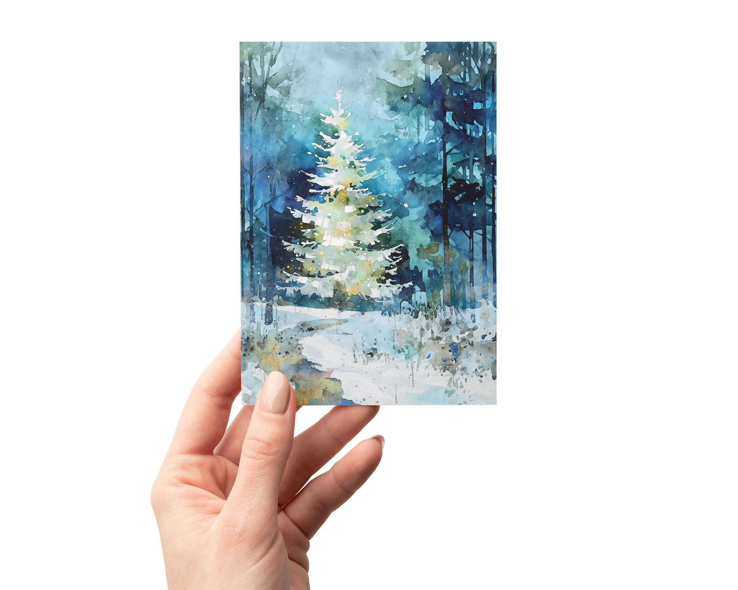 A hand holding a small greeting card featuring a watercolor painting of a glowing white Christmas tree in a snowy blue-green forest. Soft washes, tall dark tree silhouettes, and scattered light speckles create a peaceful winter scene against a clean white background.