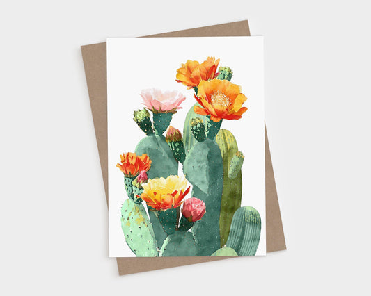 Watercolor greeting card featuring a cluster of green prickly pear cacti with vibrant blossoms in shades of orange, yellow, pink, and red, set against a white background with a kraft paper envelope behind it.