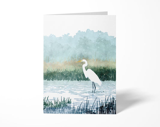 Standing greeting card featuring a watercolor-style illustration of a white egret wading in a marsh, surrounded by tall grasses and misty blue-green trees against a white background.