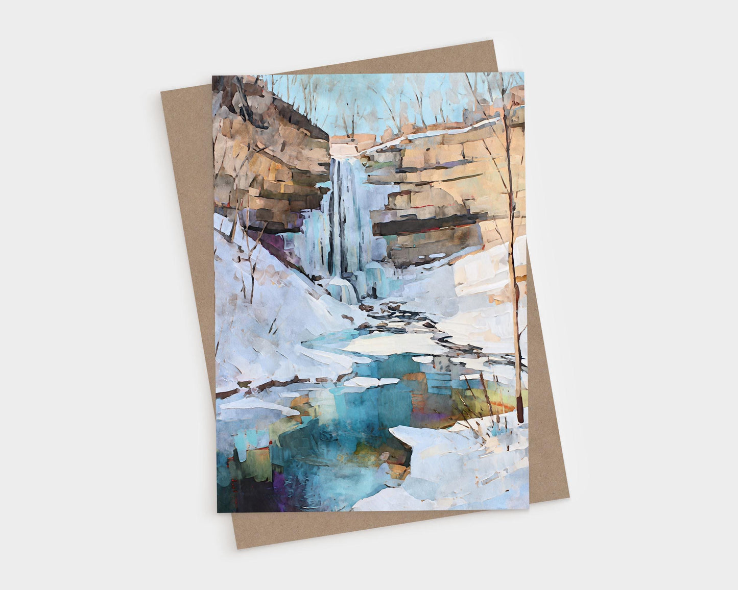 Watercolor-style greeting card featuring a winter waterfall cascading down rocky cliffs into a partially frozen pool. Snow blankets the ground and ice edges the turquoise-blue water, with bare trees silhouetted against a pale sky. A natural, serene winter landscape.