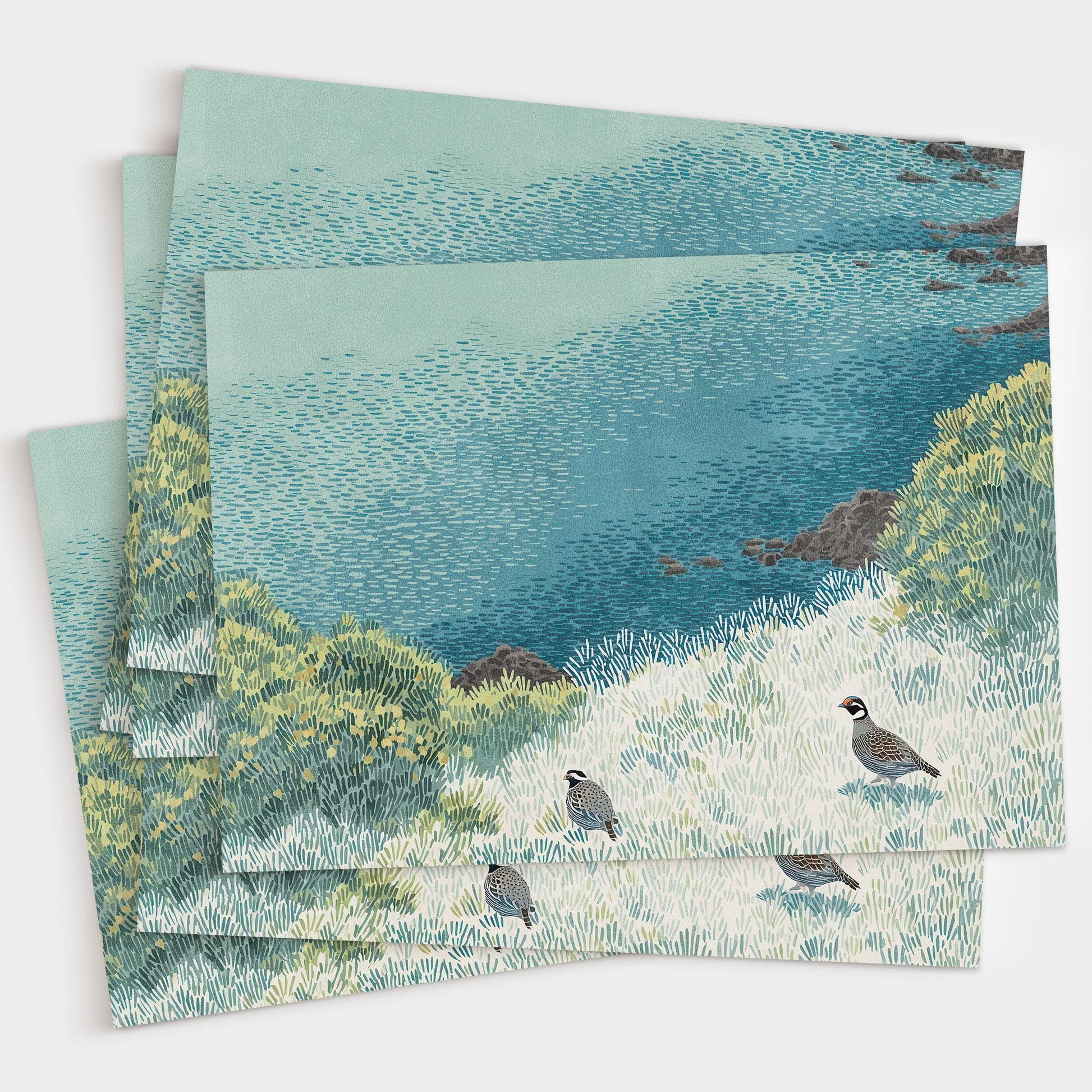 Stack of greeting cards featuring an illustration of two quail in a grassy coastal landscape with layered blue, green, and yellow textures. The cards are slightly fanned out on a white background, showcasing the detailed artwork and consistent design.