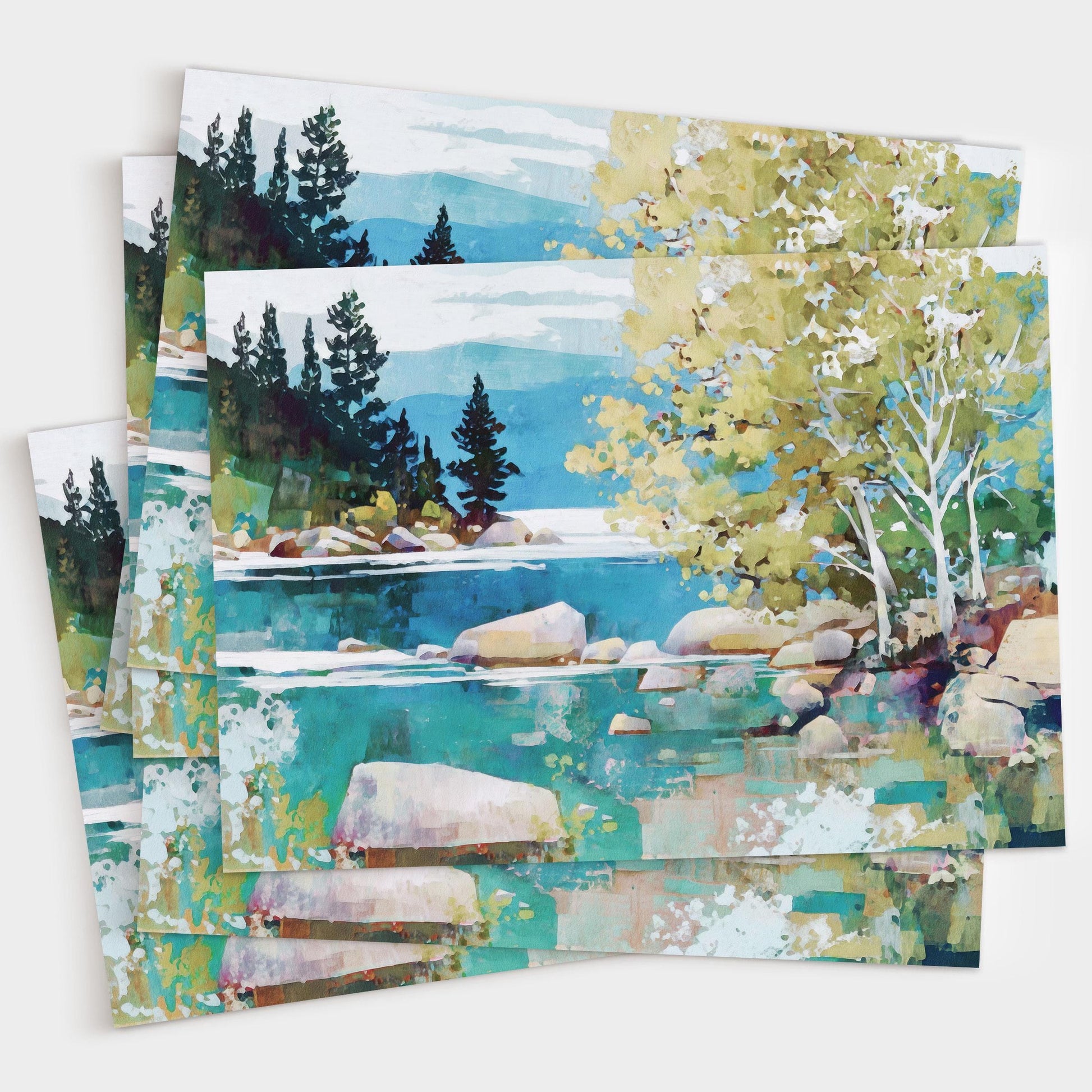 Set of greeting cards featuring a vibrant impressionist landscape of a turquoise lake with smooth boulders, birch trees with pale trunks and green foliage on the right, and dark evergreens against distant blue mountains under a cloudy sky. The cards are slightly fanned out to show multiples.
