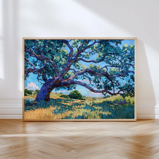 Framed art print of a sprawling Texas oak tree with twisting branches and blue-green leaves, painted in a modern impressionist style. The tree stands over golden grass under a bright blue sky with soft clouds. The artwork leans against a white wall on a light wood herringbone floor, illuminated by natural sunlight streaming through a nearby window.