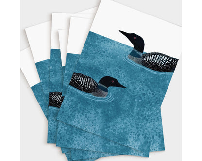 Set of vertical greeting cards featuring two loons with black-and-white plumage swimming on textured deep blue water with ripples, set against a white background, fanned out to show multiple copies.