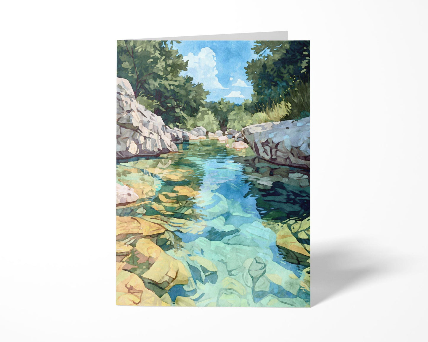 Folded greeting card featuring a watercolor-style painting of a turquoise river with golden rocks beneath the clear water, surrounded by rocky white banks and lush green trees under a blue sky with clouds. Displayed upright on a plain white background.
