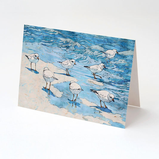 Folded greeting card featuring a watercolor-style illustration of small white shorebirds with orange legs on sand and shallow blue water, displayed upright against a clean white background.