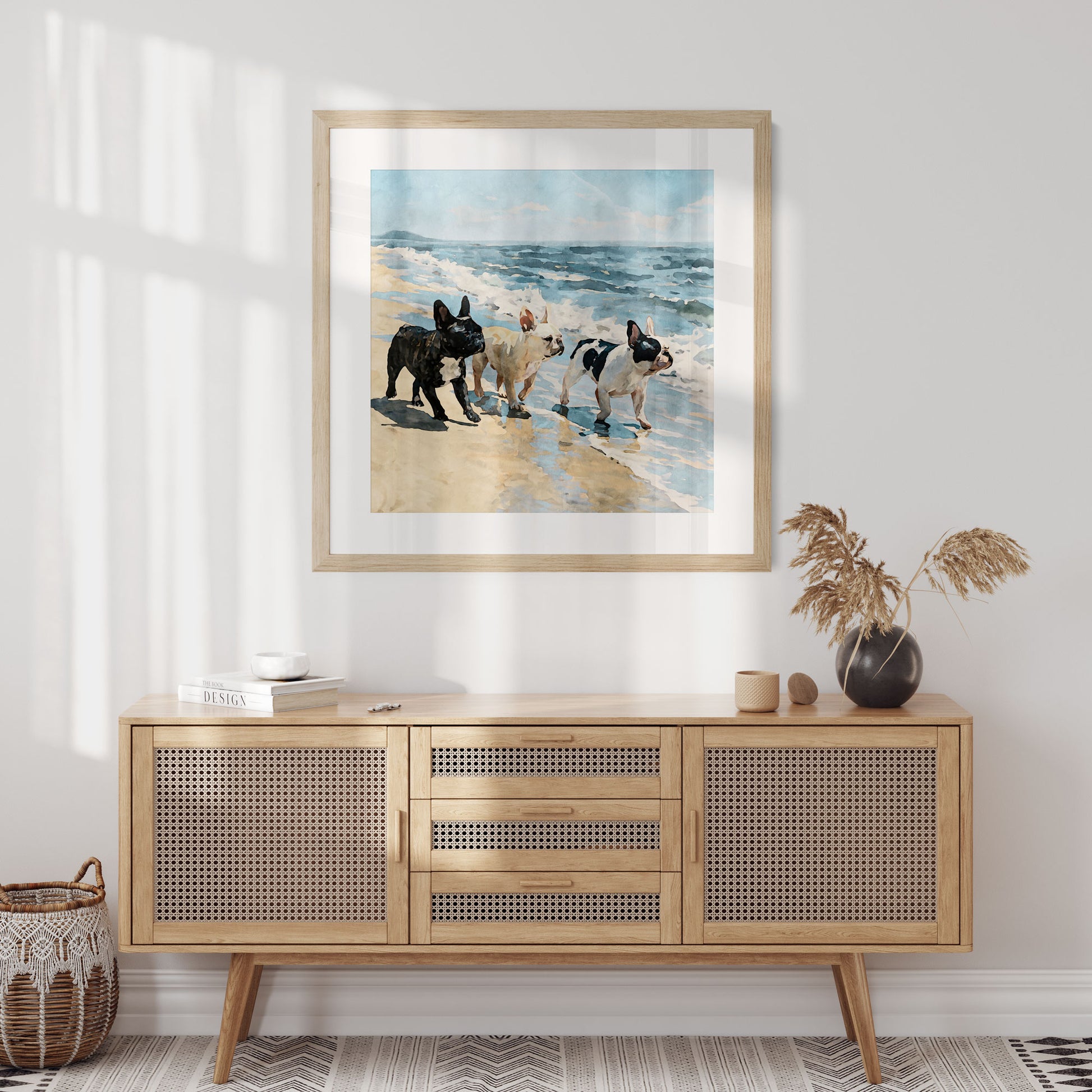 Square framed beach watercolor print featuring three French Bulldogs by blue ocean waves in a styled interior.