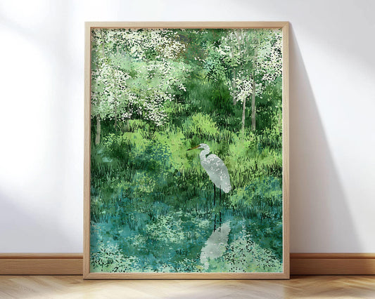 Framed art print of a serene watercolor-style illustration featuring a white egret standing by a still pond, reflected in the water below. The background is lush with textured green grasses and trees dappled in soft white blossoms, evoking a peaceful springtime woodland scene.