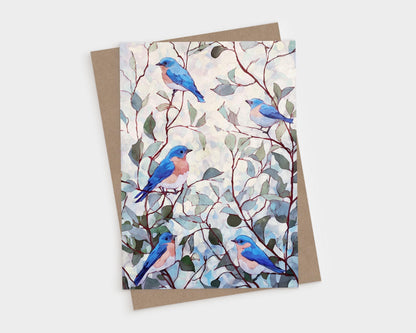 Watercolor greeting card featuring five bluebirds with peachy chests perched among delicate branches and muted green leaves against a softly dappled background, paired with a brown kraft envelope.