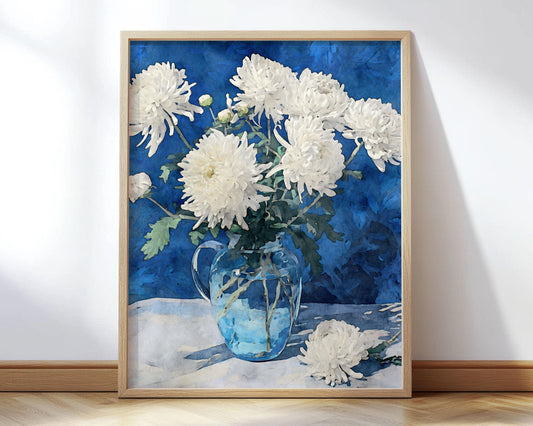 Framed art print of white chrysanthemums arranged in a clear glass pitcher, set against a deep blue background. One flower lies on the table beside the vase, creating a serene still life composition.