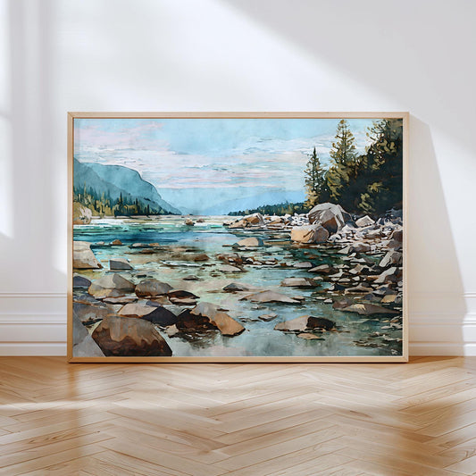 Framed watercolor landscape painting of a rocky mountain river under a soft blue and pink sky. The clear turquoise water flows between large stones, with pine trees and forested cliffs rising on the right and distant misty peaks in the background. The artwork leans against a white wall on a light wood herringbone floor, illuminated by natural sunlight.