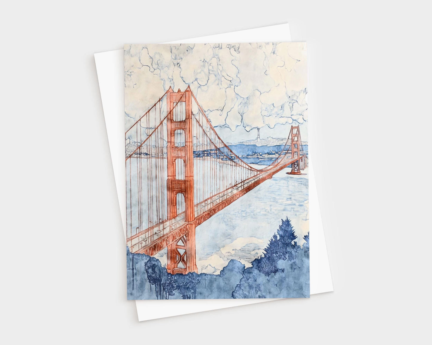 Greeting card featuring a watercolor illustration of the Golden Gate Bridge in warm terra-cotta tones, stretching across a pale blue bay. Billowing clouds fill the sky above, with soft washes of navy and indigo detailing the foliage in the foreground and the San Francisco skyline in the distance.