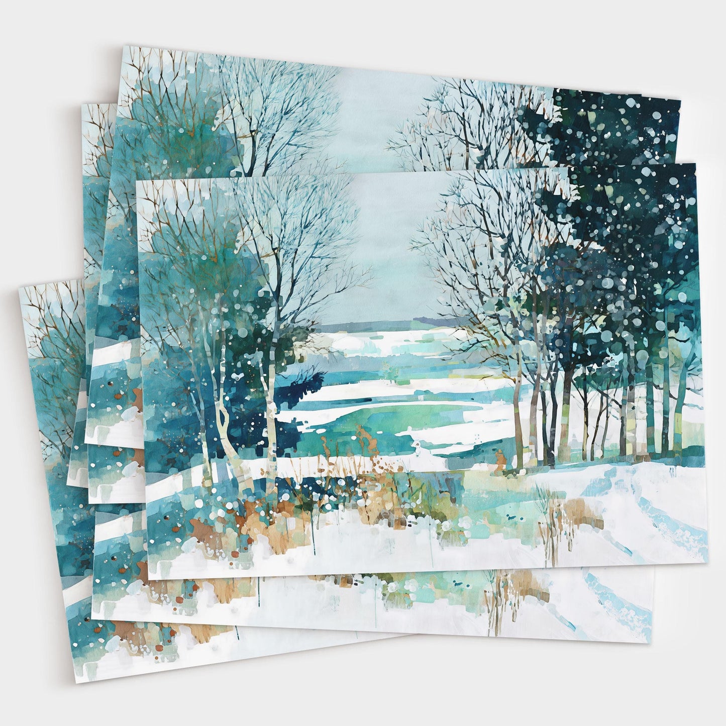 Set of watercolor greeting cards featuring a serene winter landscape with snowy fields, bare trees, and evergreens in teal, blue, and white, with splattered paint details suggesting falling snow. Cards are stacked in a fanned arrangement.