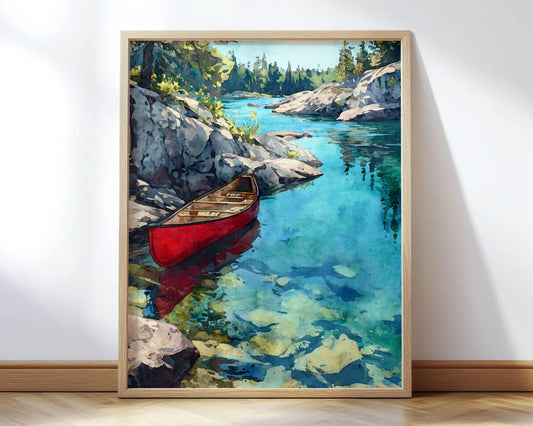 Framed art print of a red canoe resting in clear turquoise water along a rocky shoreline. Sunlit stone cliffs rise on the left, casting shadows into the shallows. The vibrant water reveals smooth rocks beneath the surface, and distant pines line the horizon under a bright sky. The print leans against a white wall on a light wood floor.