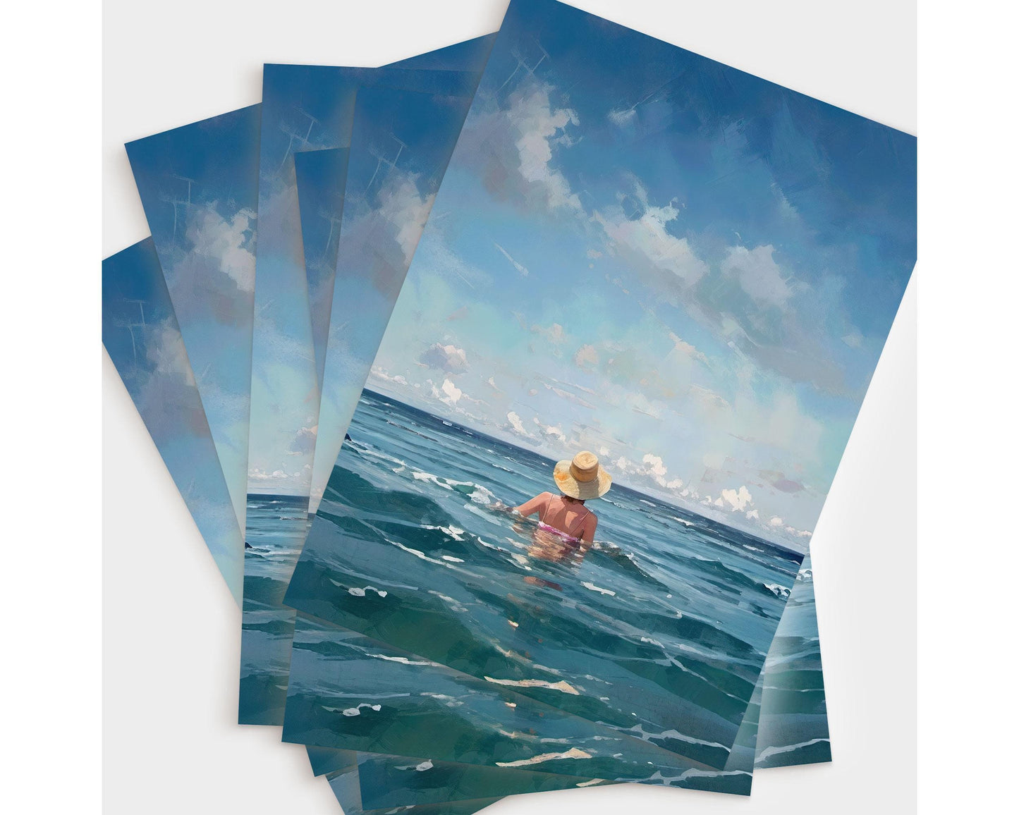 A fanned-out stack of ocean-themed greeting cards featuring a woman in a straw hat wading into the sea, shown from behind against a vivid blue sky.