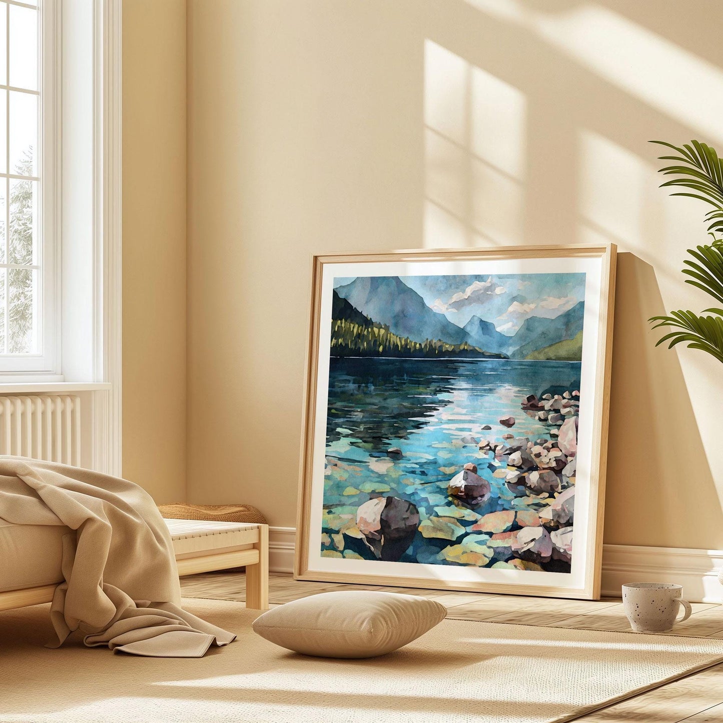 Framed watercolor painting of a clear mountain lake with colorful submerged rocks, pine-covered shoreline, and distant blue mountains under a partly cloudy sky, leaning against a wall in a sunlit, minimalist bedroom with beige tones.