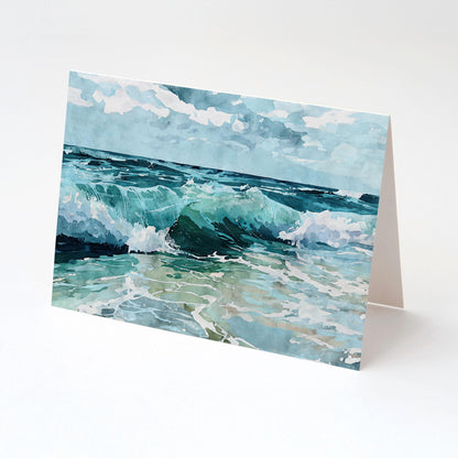 Folded greeting card featuring a watercolor seascape of turquoise waves crashing onto the shore beneath a partly cloudy sky, displayed upright against a plain white background.
