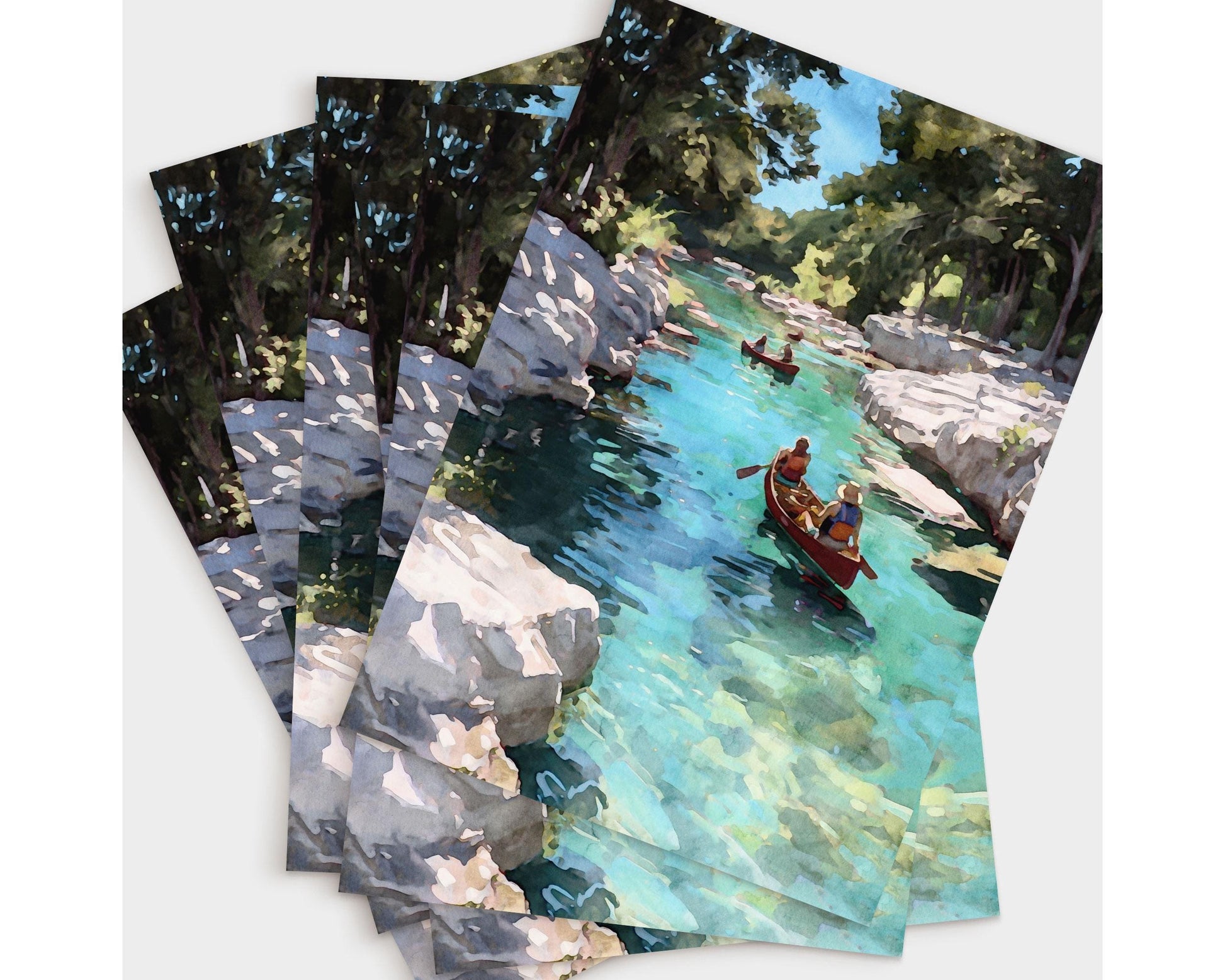 Set of greeting cards featuring a watercolor-style painting of two red canoes on a clear turquoise river, framed by rocky white banks and green trees under a bright blue sky, fanned out in a layered display.