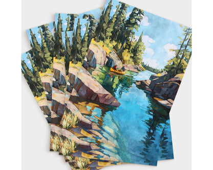 Set of greeting cards featuring a watercolor painting of a golden canoe on a turquoise lake, surrounded by rocky cliffs and tall pine trees under a bright sky. The cards are fanned out, showing multiple copies of the same wilderness scene.