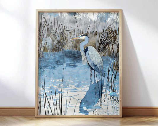 Framed watercolor-style art print of a heron standing in shallow blue water surrounded by tall marsh grasses, with its reflection visible in the rippling surface. The piece features cool tones of blue and gray with earthy brown accents, creating a serene wetland scene.